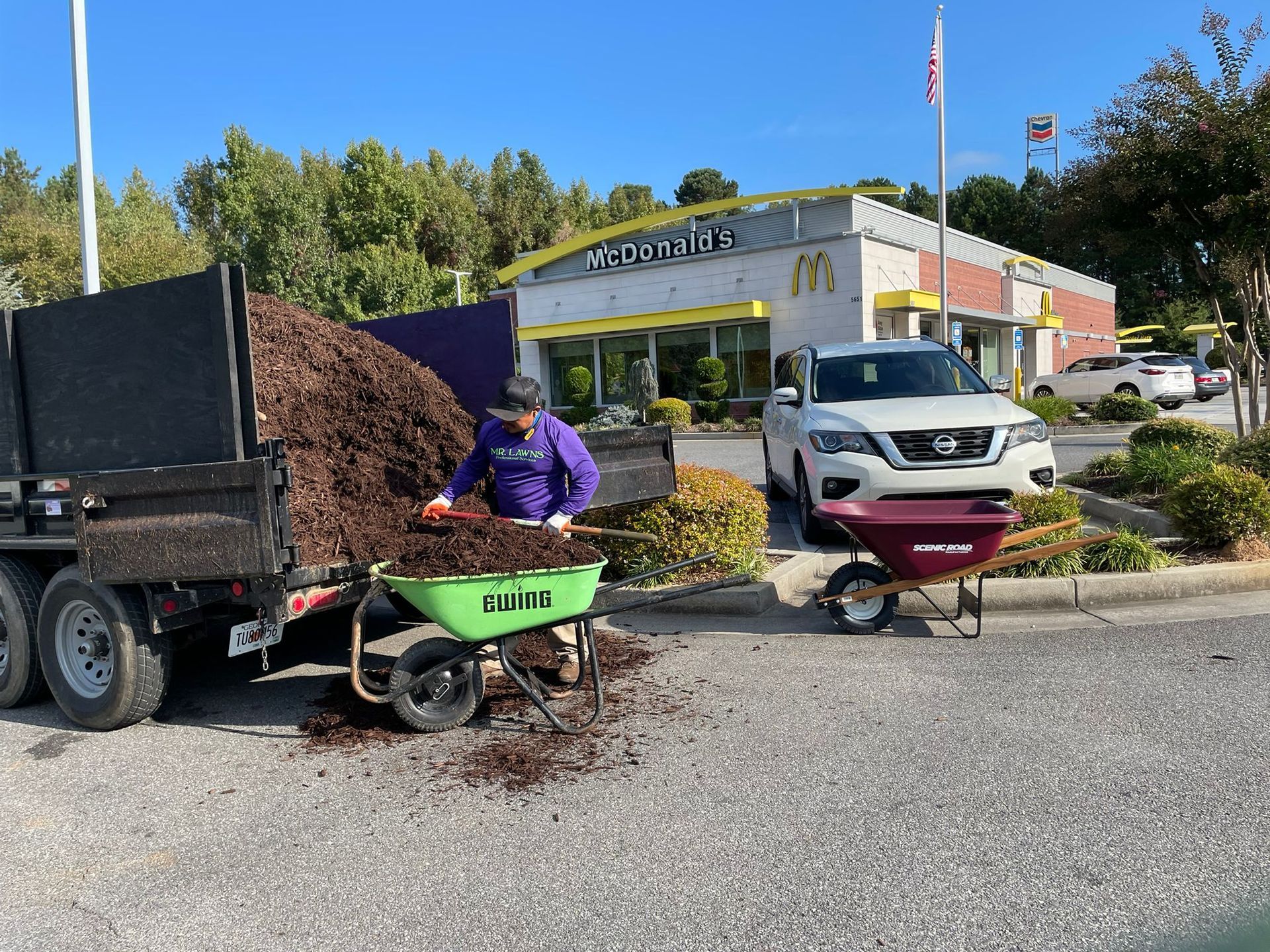 Person shoveling mulch from a trailer into wheelbarrows at a McDonald's.