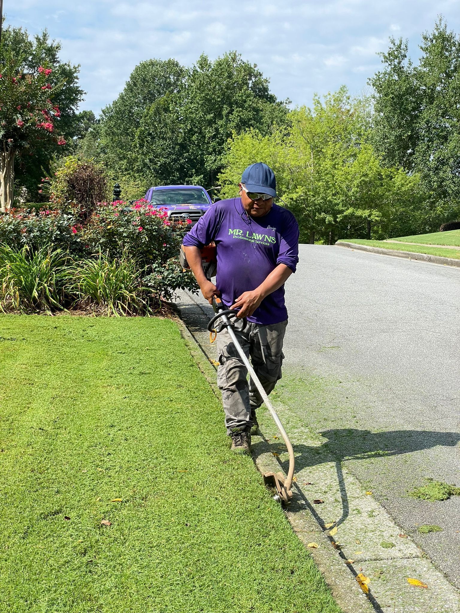 Man using weed eater to trim grass along a driveway.