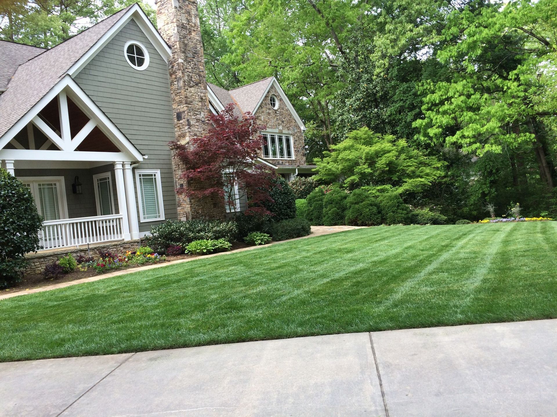 House with manicured lawn, stone chimney, and trees in a residential setting.