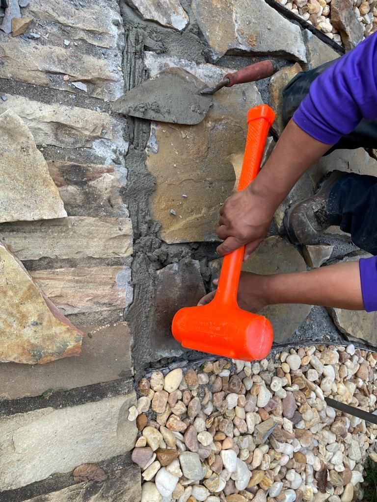 Person using a mallet to secure stones in a stone wall, orange mallet, concrete.