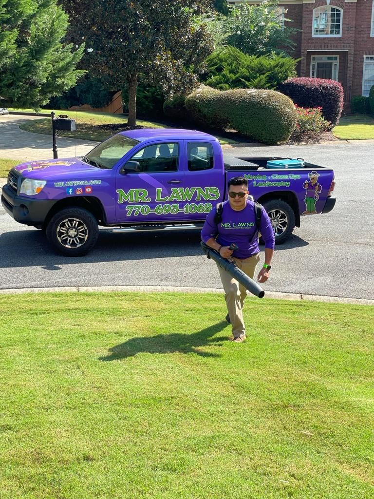 Man with a leaf blower in front of a purple truck, in a yard.