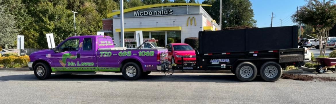 Purple truck with a trailer, in front of a McDonald's. A red car is parked in between.