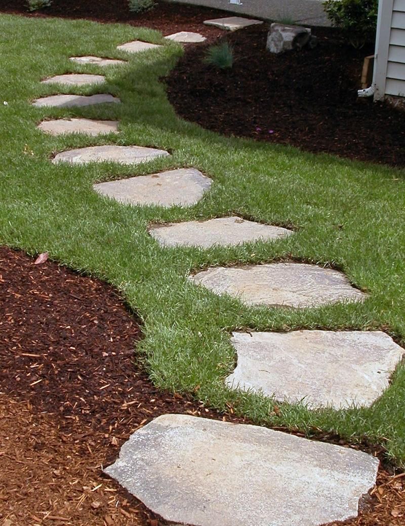 Stone path winding through green grass and dark mulch.
