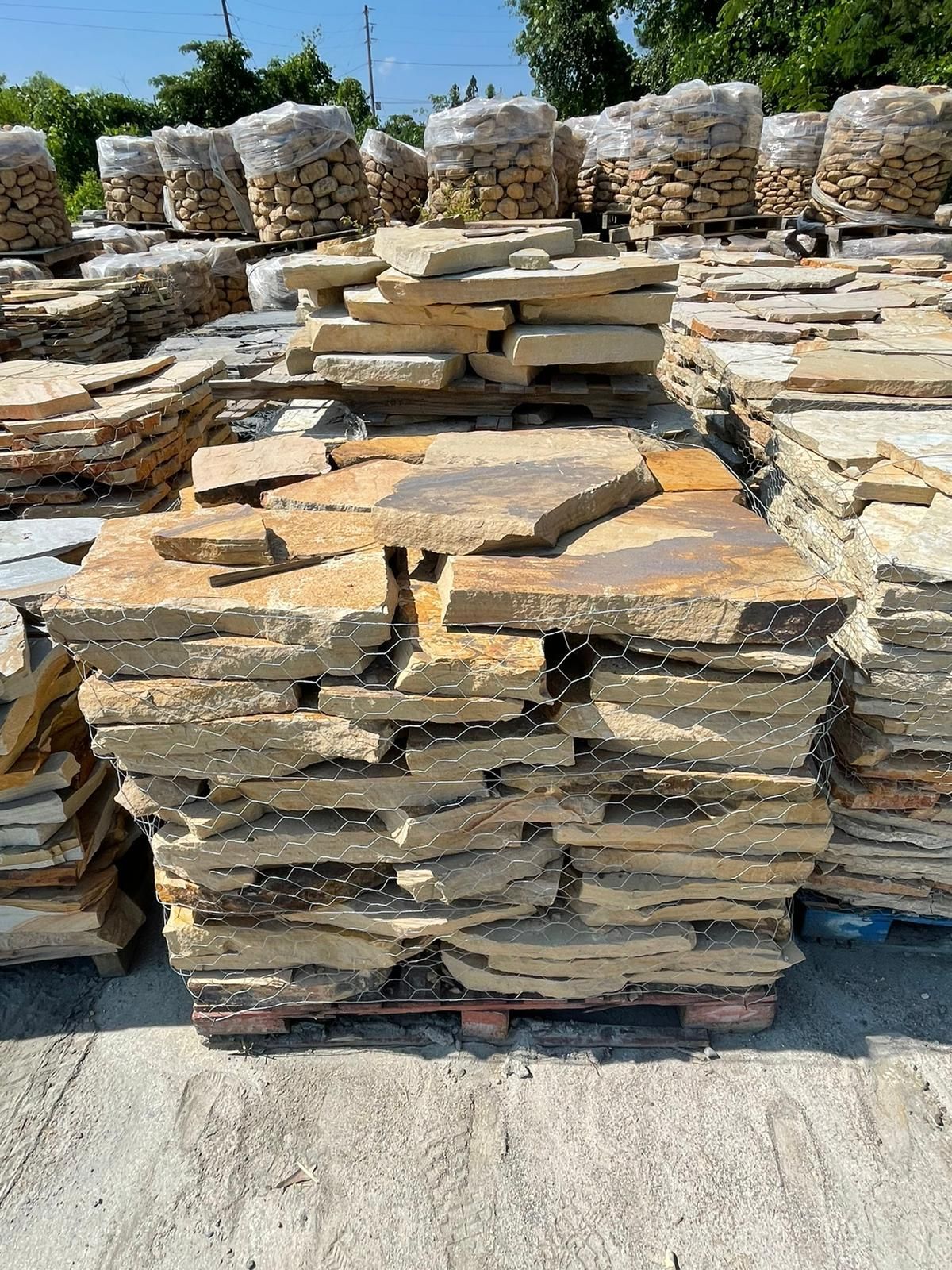 Stacks of irregularly shaped, tan-colored flagstones on a wooden pallet outdoors.