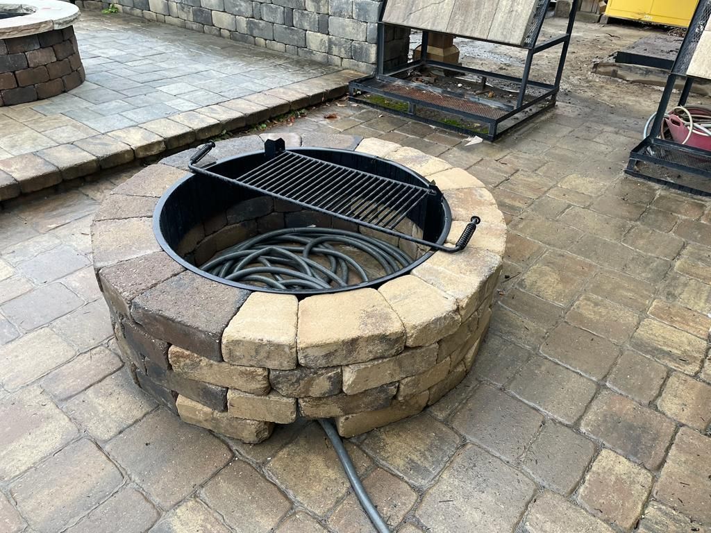 Circular brick fire pit with metal grill on a stone patio.