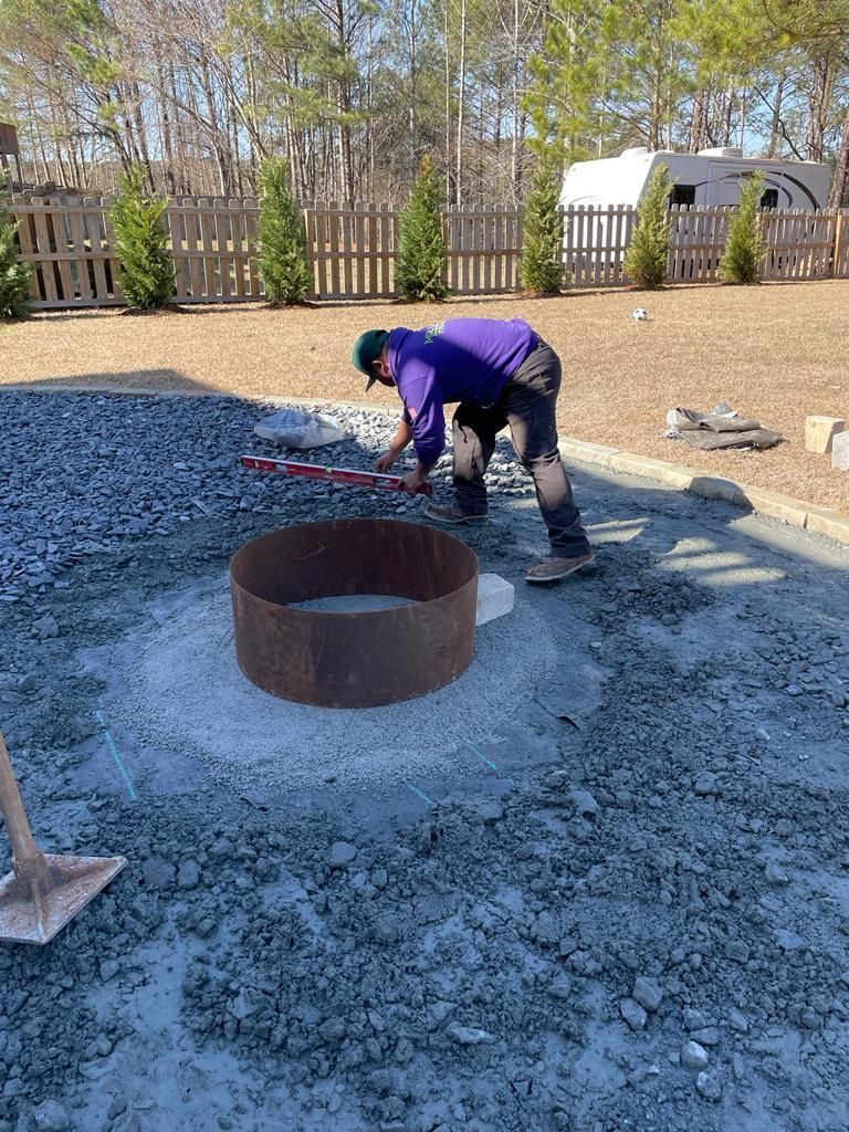 Man building fire pit in yard; gravel, metal ring, level in use; sunny day.