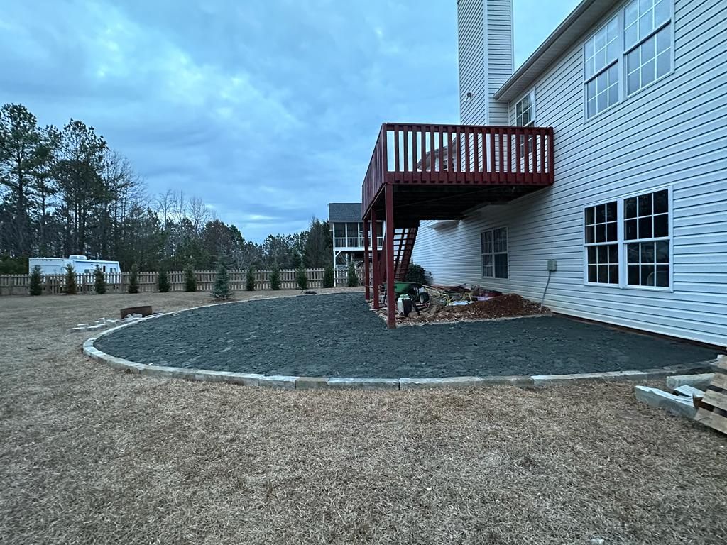 Backyard with a raised deck, gravel bed, and evergreen trees. Overcast sky.