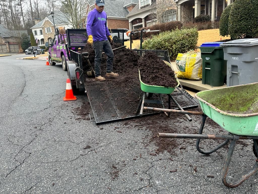 Man shoveling mulch from a trailer into a wheelbarrow on a residential street.