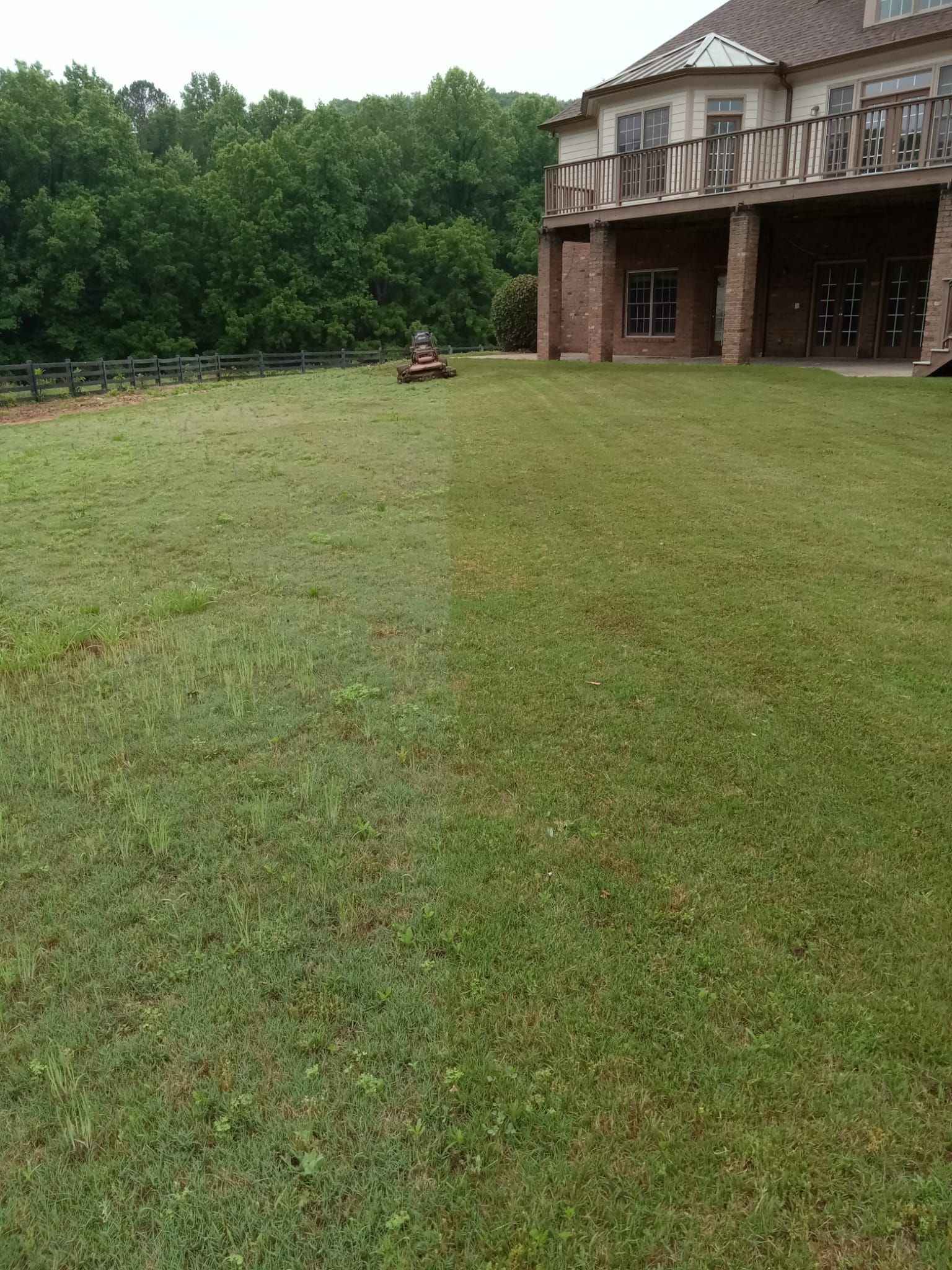 Lawn being mowed with a riding lawnmower in front of a large house with a balcony.