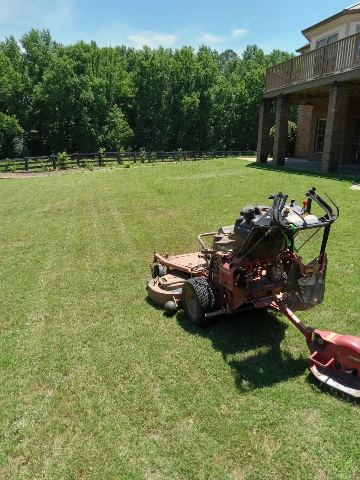 Lawnmower on a green lawn with a house in the background and a fence in the distance. Sunny day.