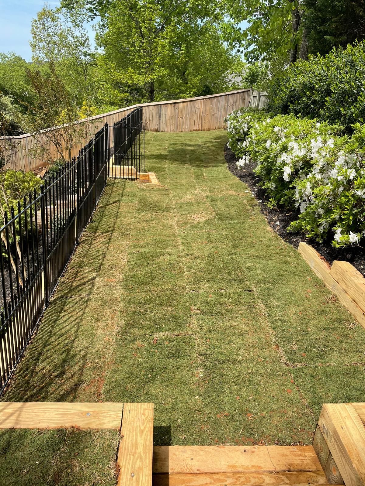 Lawn and garden path with wooden steps, black fence, and retaining wall.