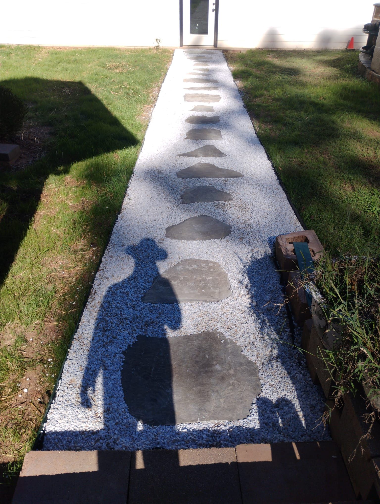 Stone path with stepping stones leading to a door; a person's shadow is cast on the path.