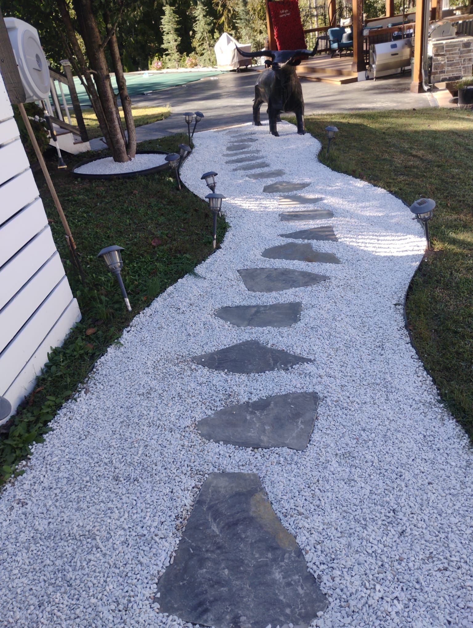 Stone path winding through white gravel, bordered by green grass and solar lights.