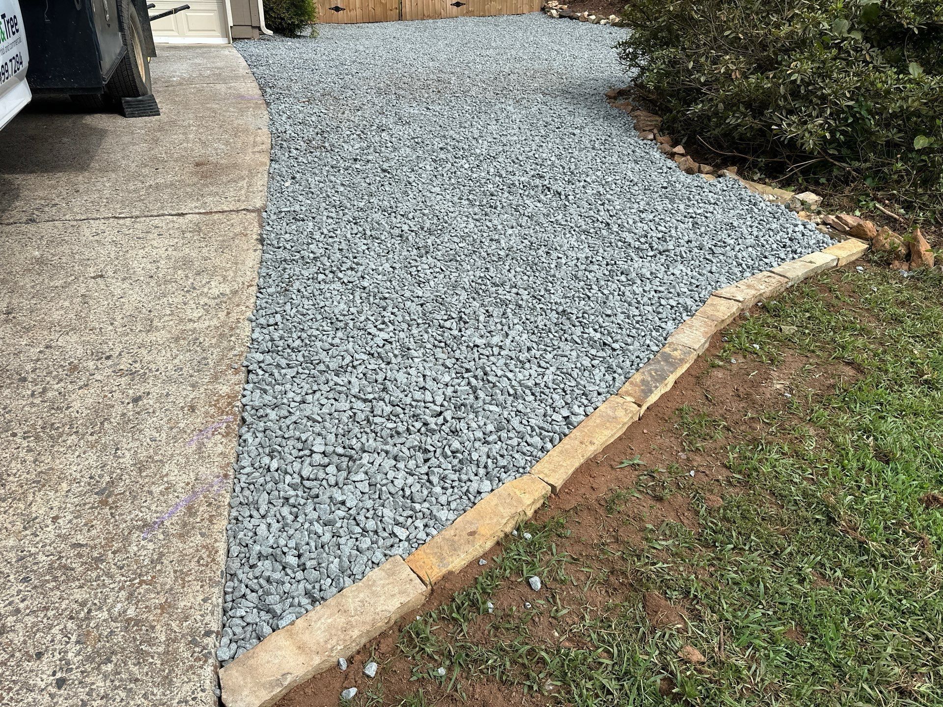 Gravel pathway bordered by stone, adjacent to a concrete sidewalk and lawn.