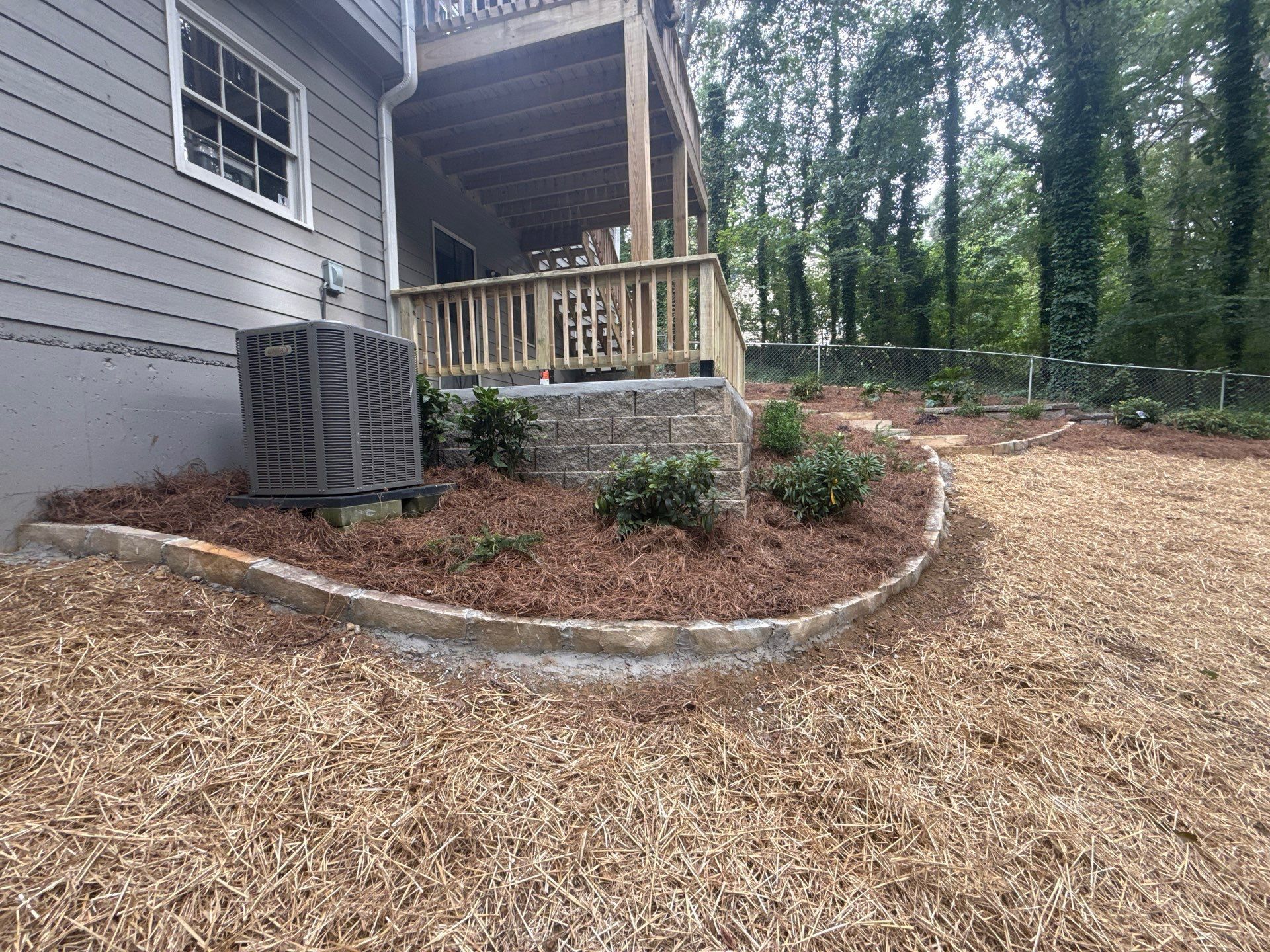Exterior of house with deck, air conditioning unit, and landscaped bed.