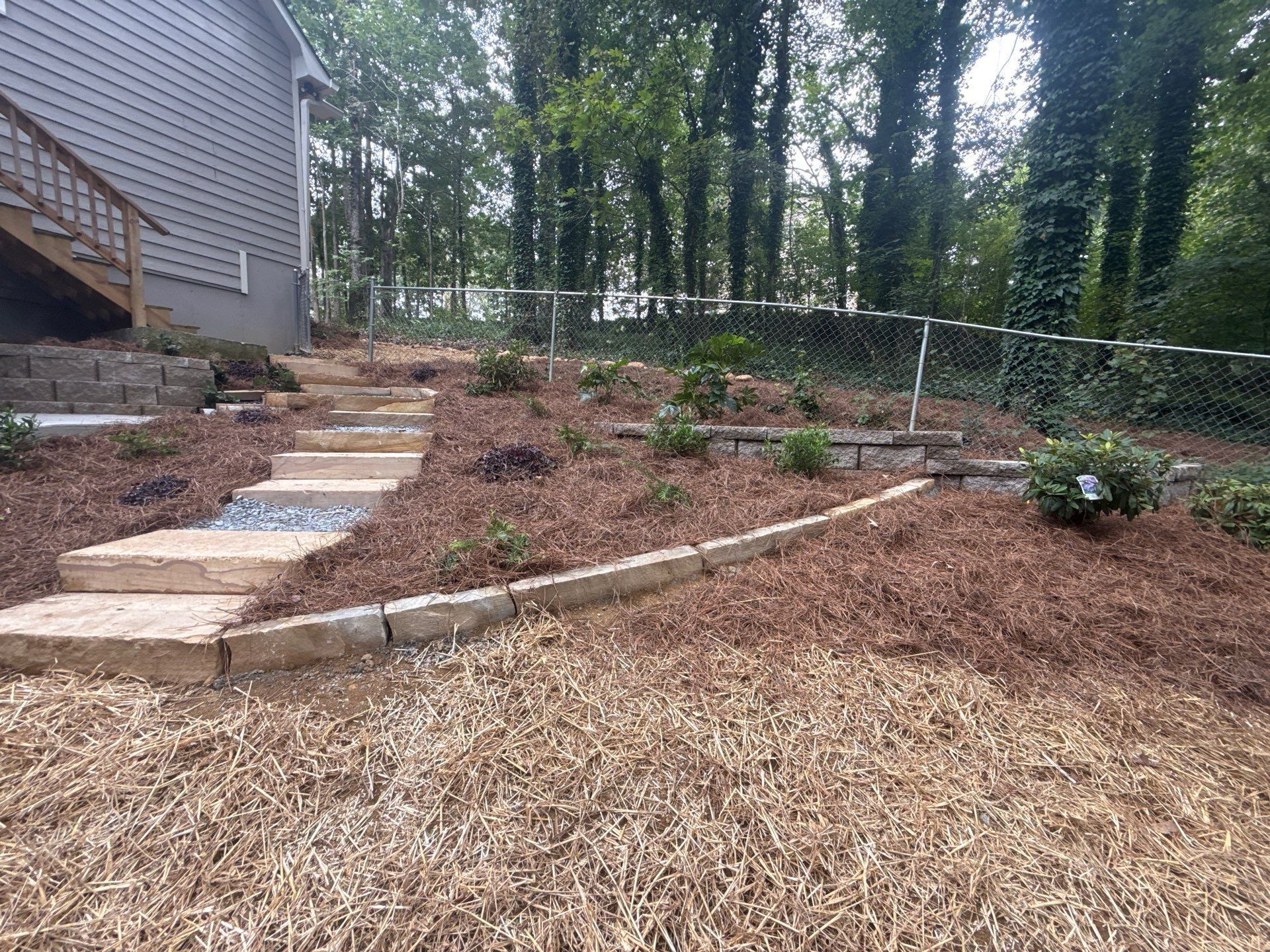Steps leading uphill in a landscaped yard, with a building on the left and trees in the background.