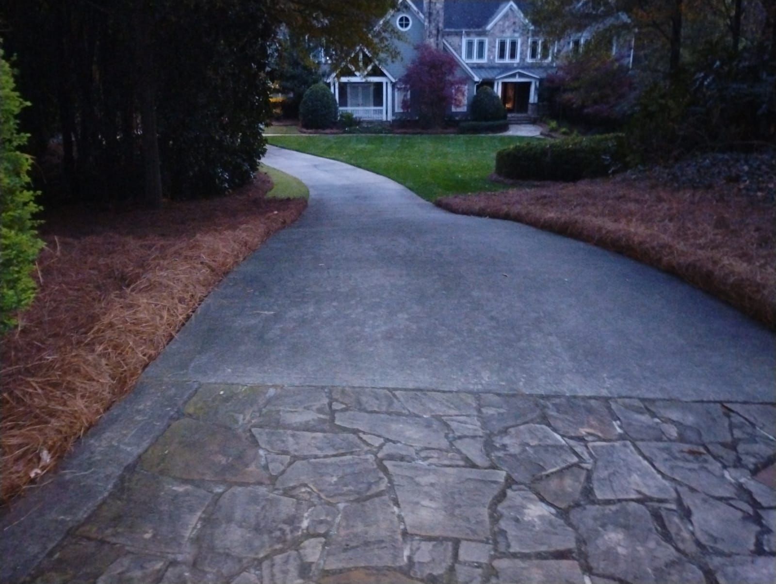 Driveway leading to a large house; concrete and stone with brown mulch borders.
