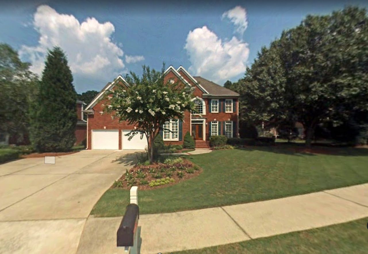 Two-story red brick house with a garage, front yard, and driveway under a blue sky with clouds.