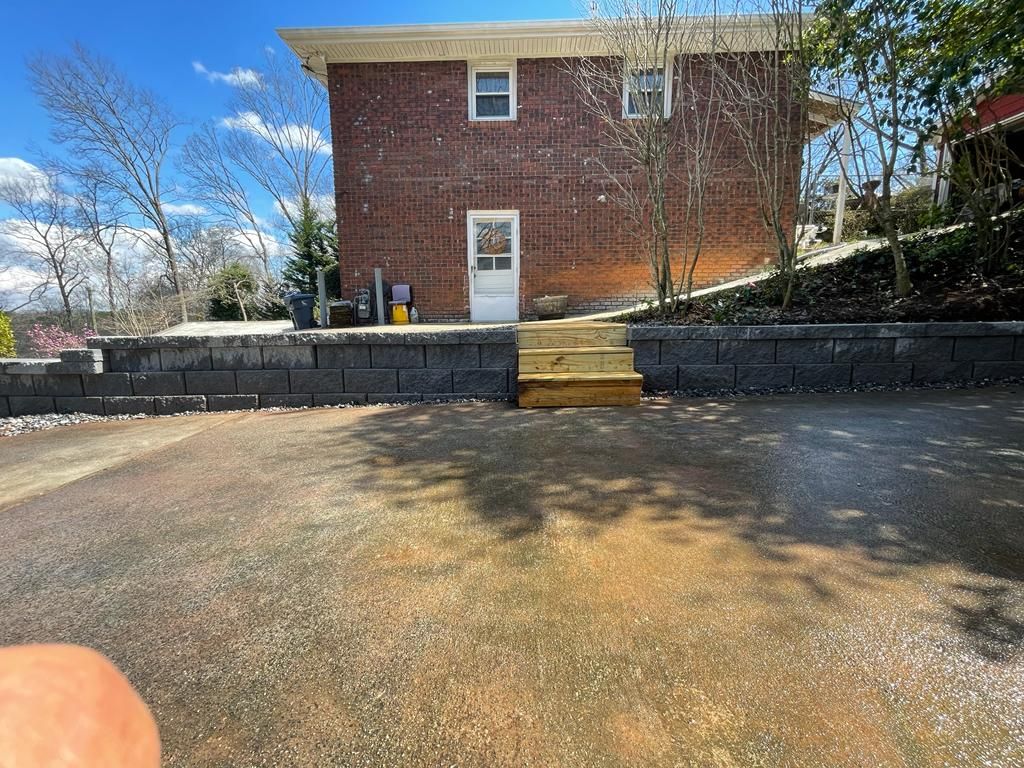 Brick house exterior with retaining wall, wooden steps, and driveway under a blue sky.