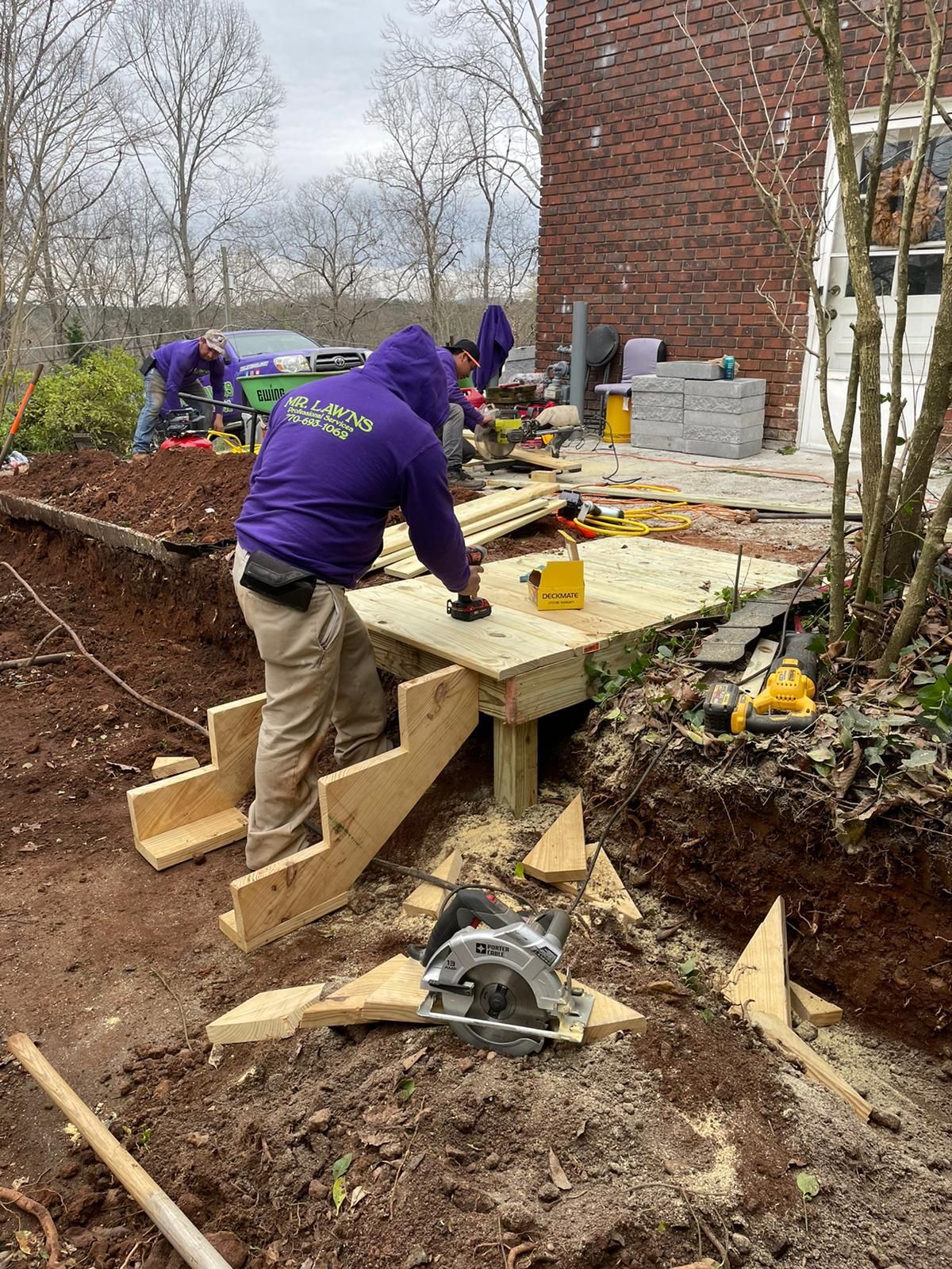 Construction workers building a wooden deck and stairs next to a brick building.