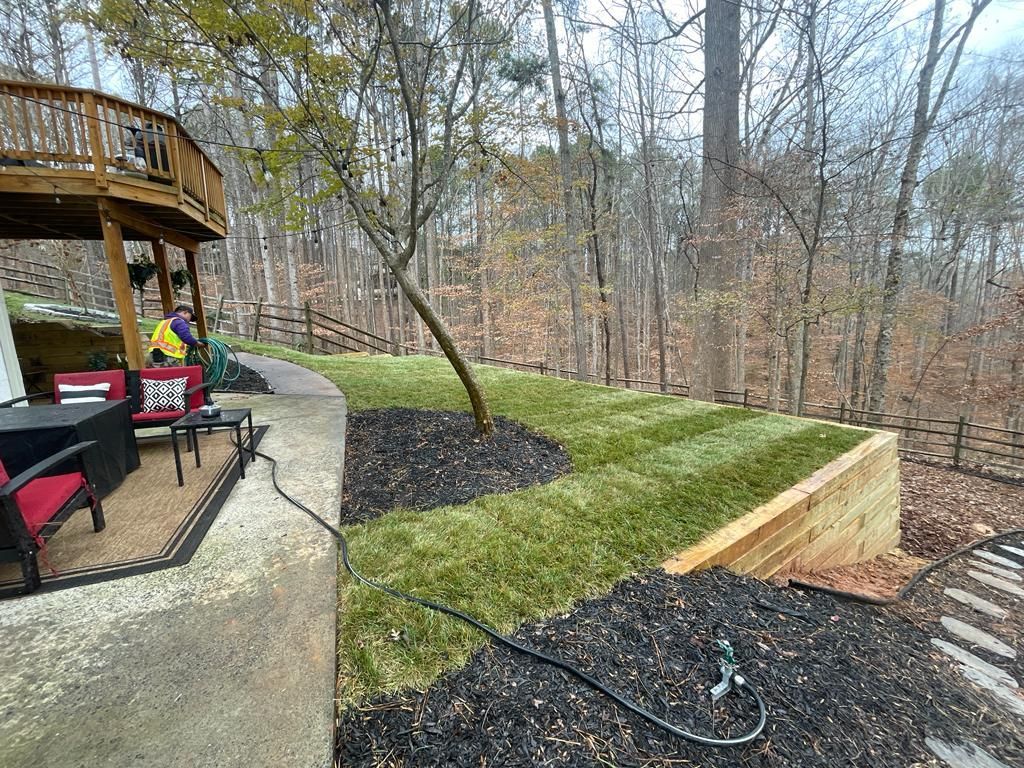 Backyard with tiered lawn, wooden deck, retaining walls, trees, and outdoor seating.