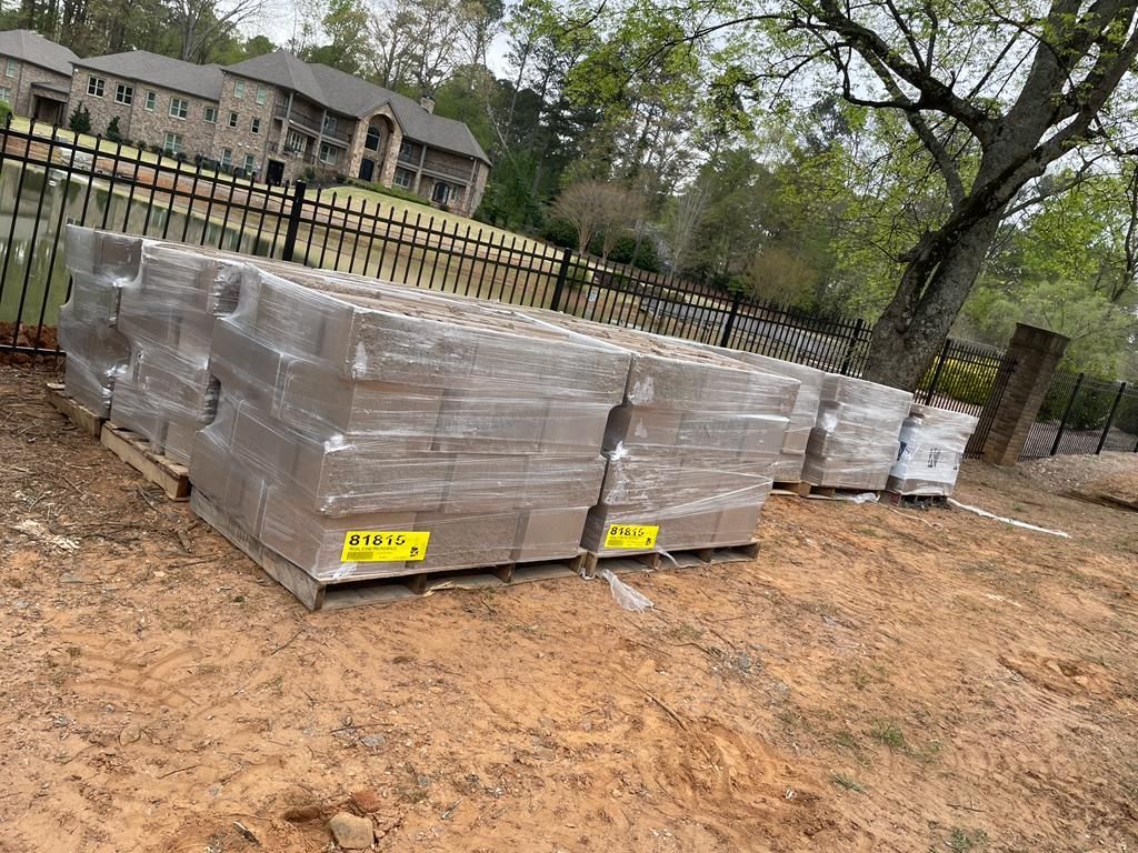 Pallets of gray concrete blocks wrapped in plastic, outdoors.