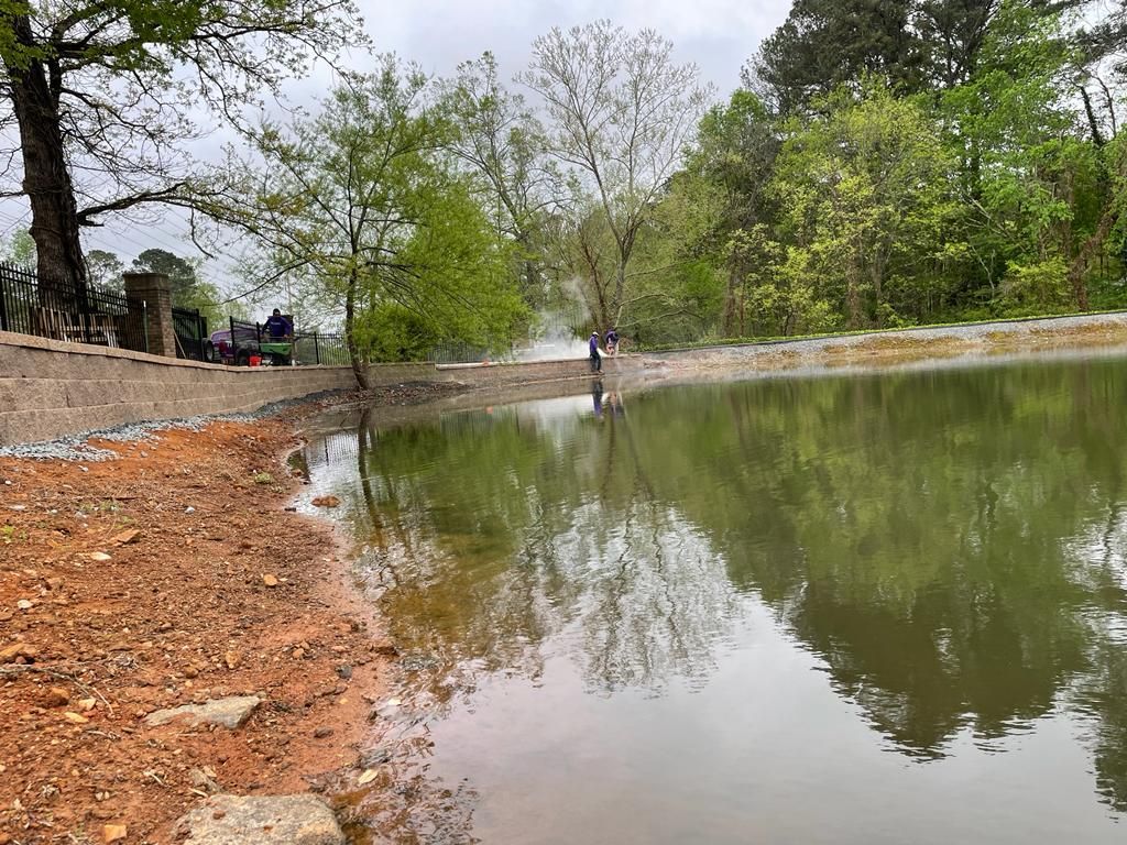 A pond reflecting trees and sky, with a person standing at the water's edge on a cloudy day.