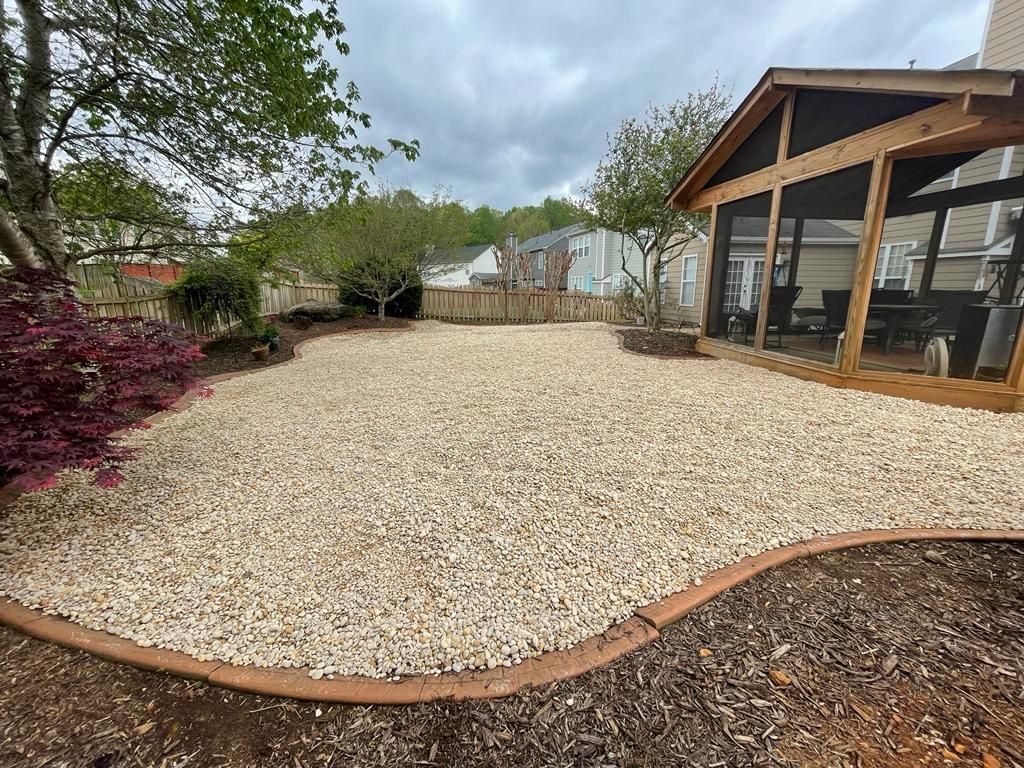 Backyard with gravel ground cover, bordered by a brown edging and landscaping near a screened porch.