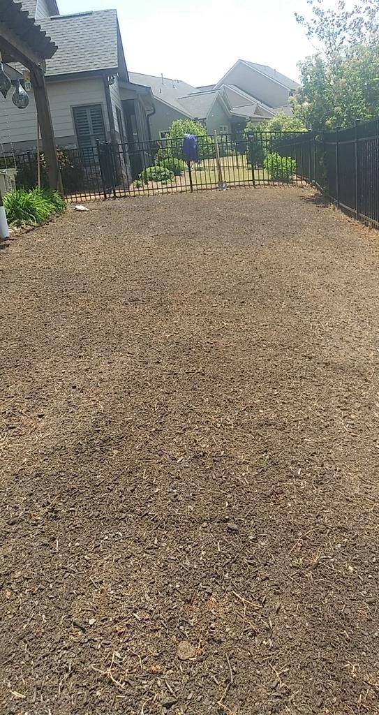 Gravel-covered backyard, long and rectangular, surrounded by a fence, house, and some greenery.