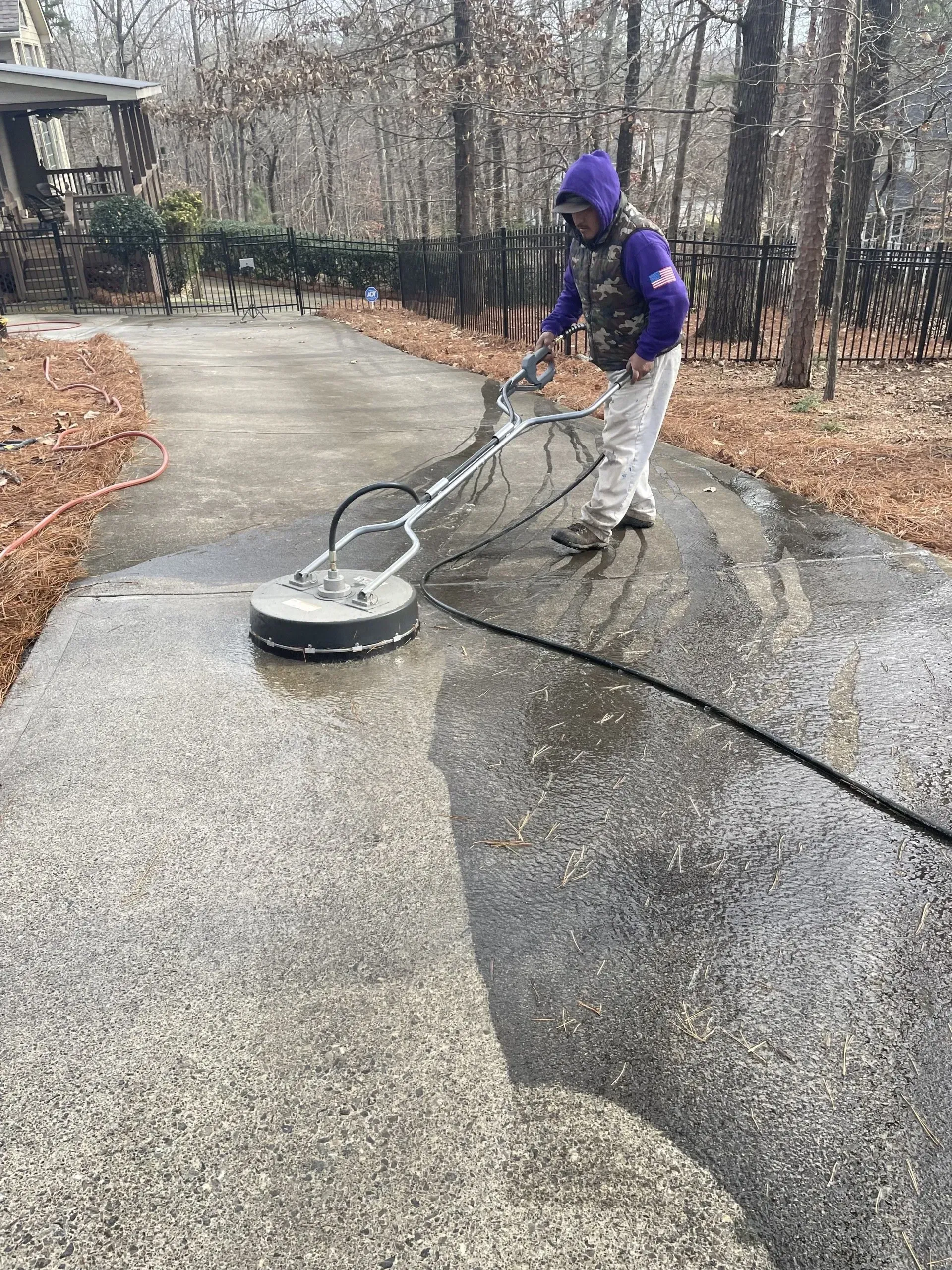 Person in purple camo jacket pressure washing a concrete driveway.