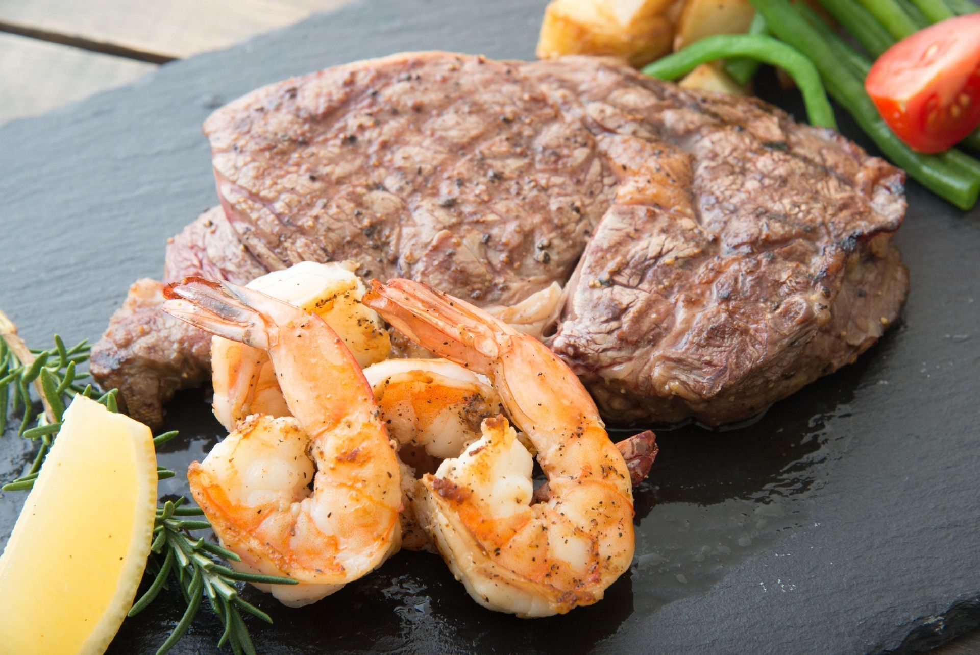 Grilled steak with shrimp, lemon wedge, and vegetables on a dark plate