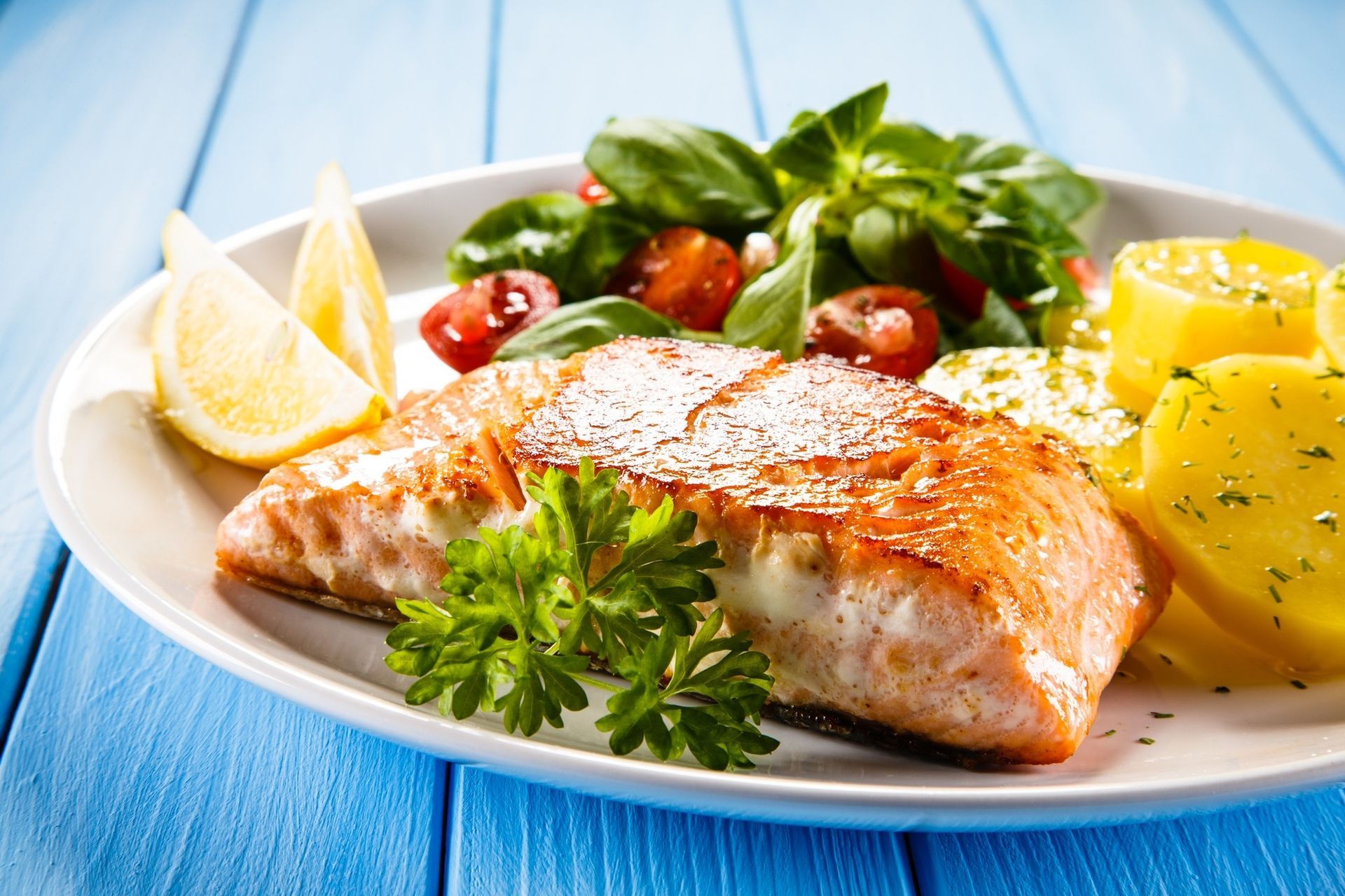Grilled salmon with lemon, potatoes, and greens on a white plate