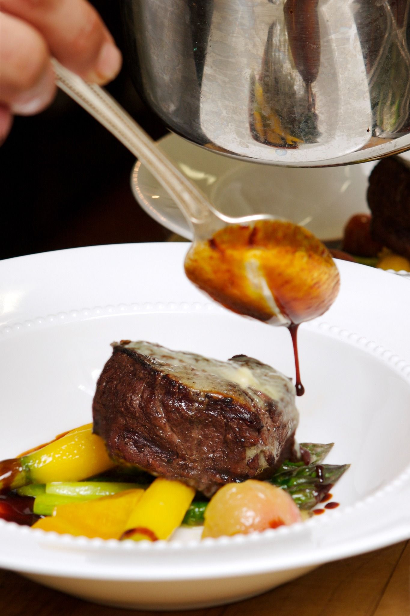 Chef spooning sauce over a plated steak with vegetables