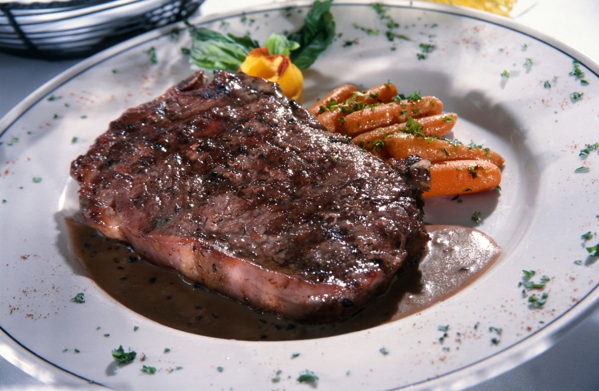 Grilled steak on a white plate with carrots and parsley garnish