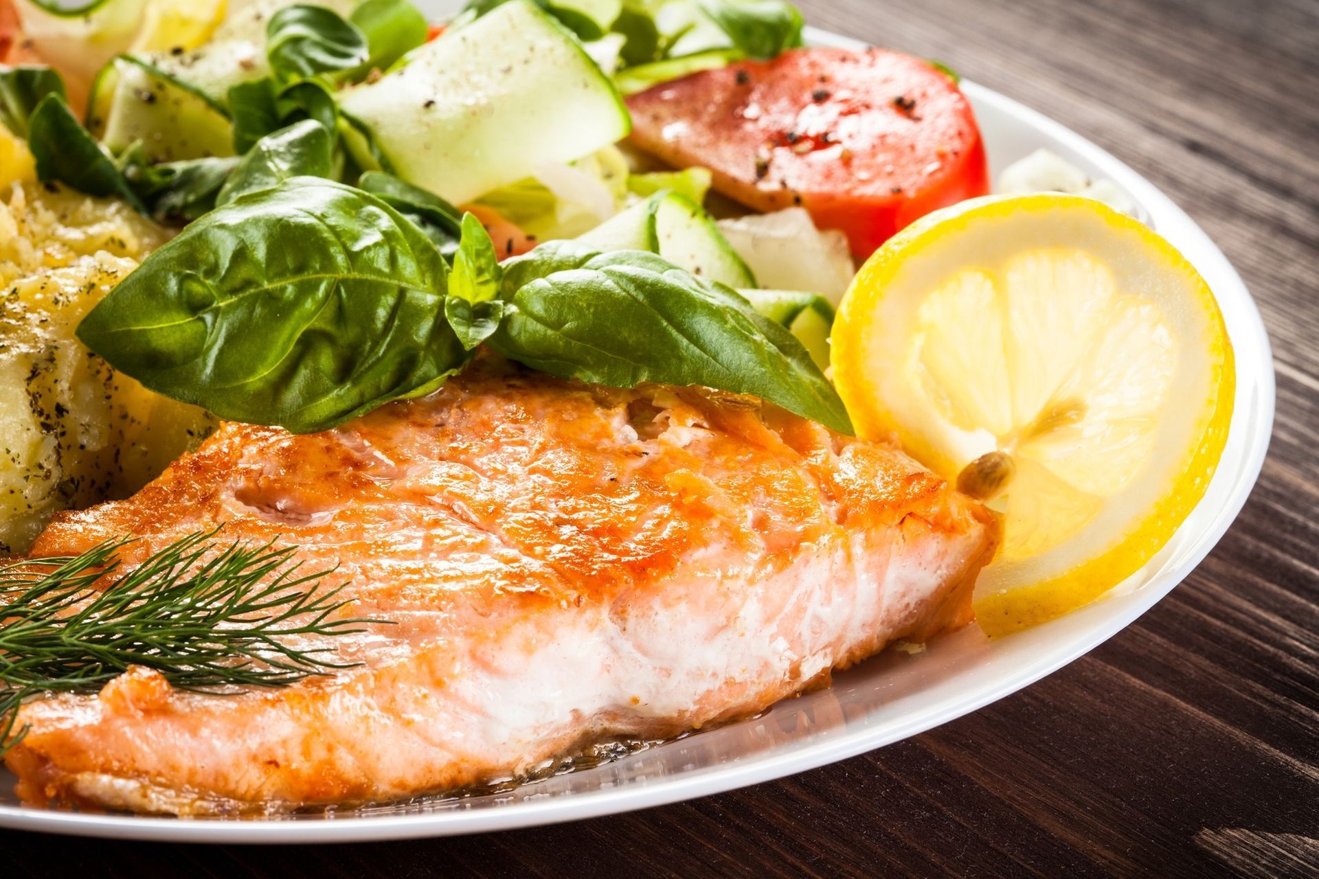 Grilled salmon with basil, lemon slice, and fresh salad on a white plate