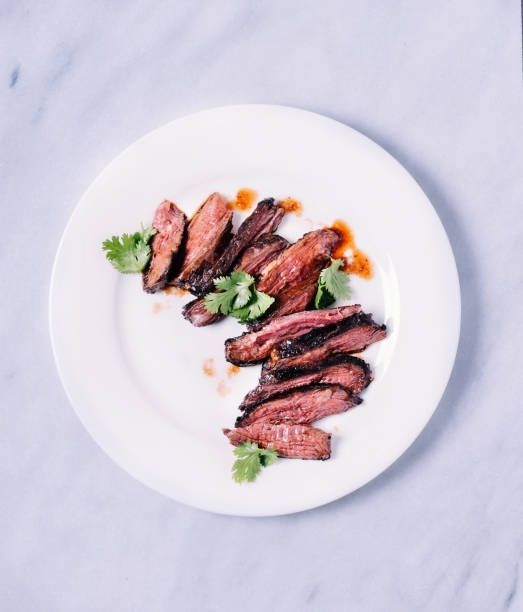 Plated sliced grilled meat with herbs and sauce on a white plate