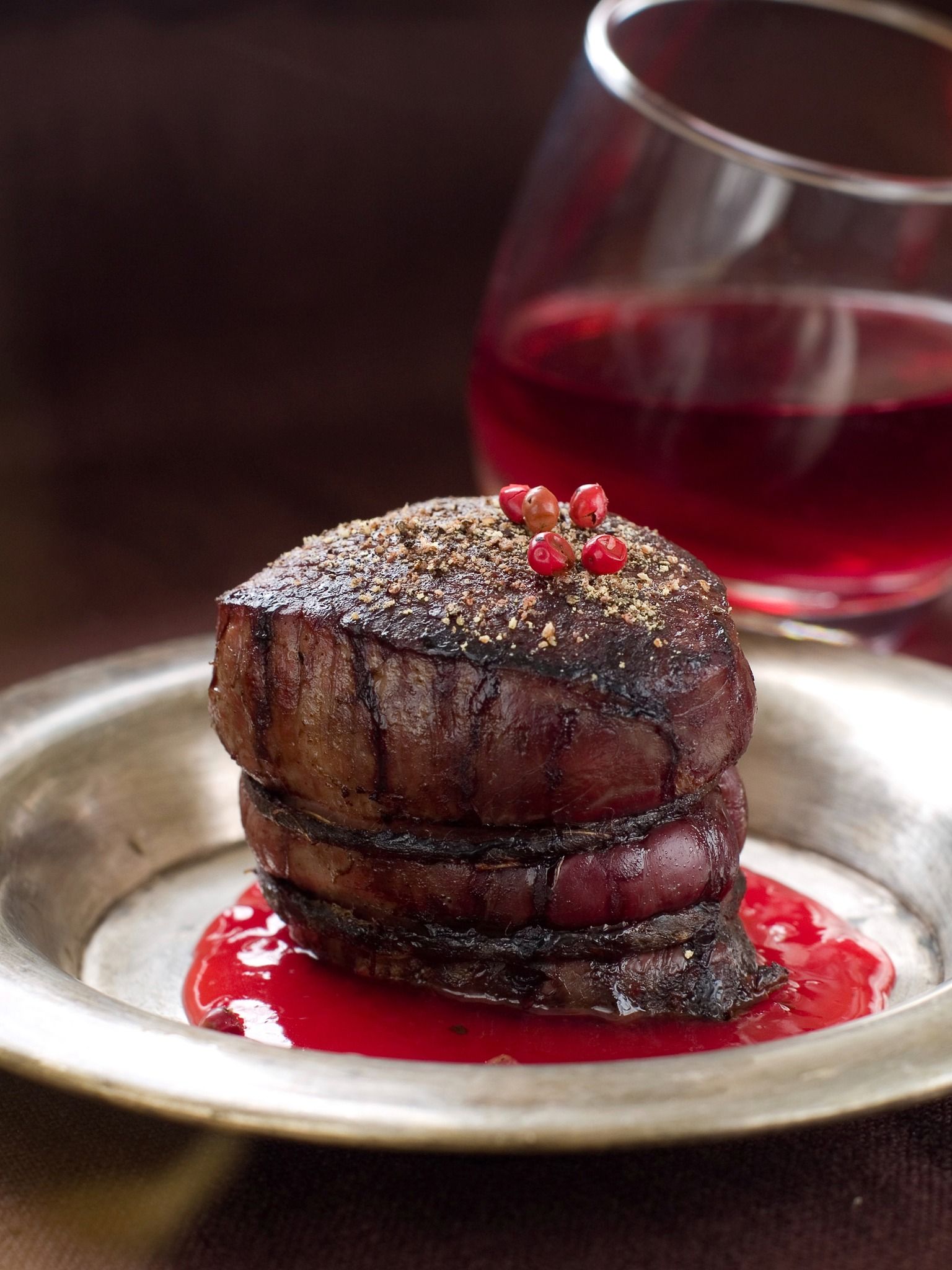 Chocolate dessert with berry sauce on a plate, topped with red berries and powdered sugar, beside a glass of red wine