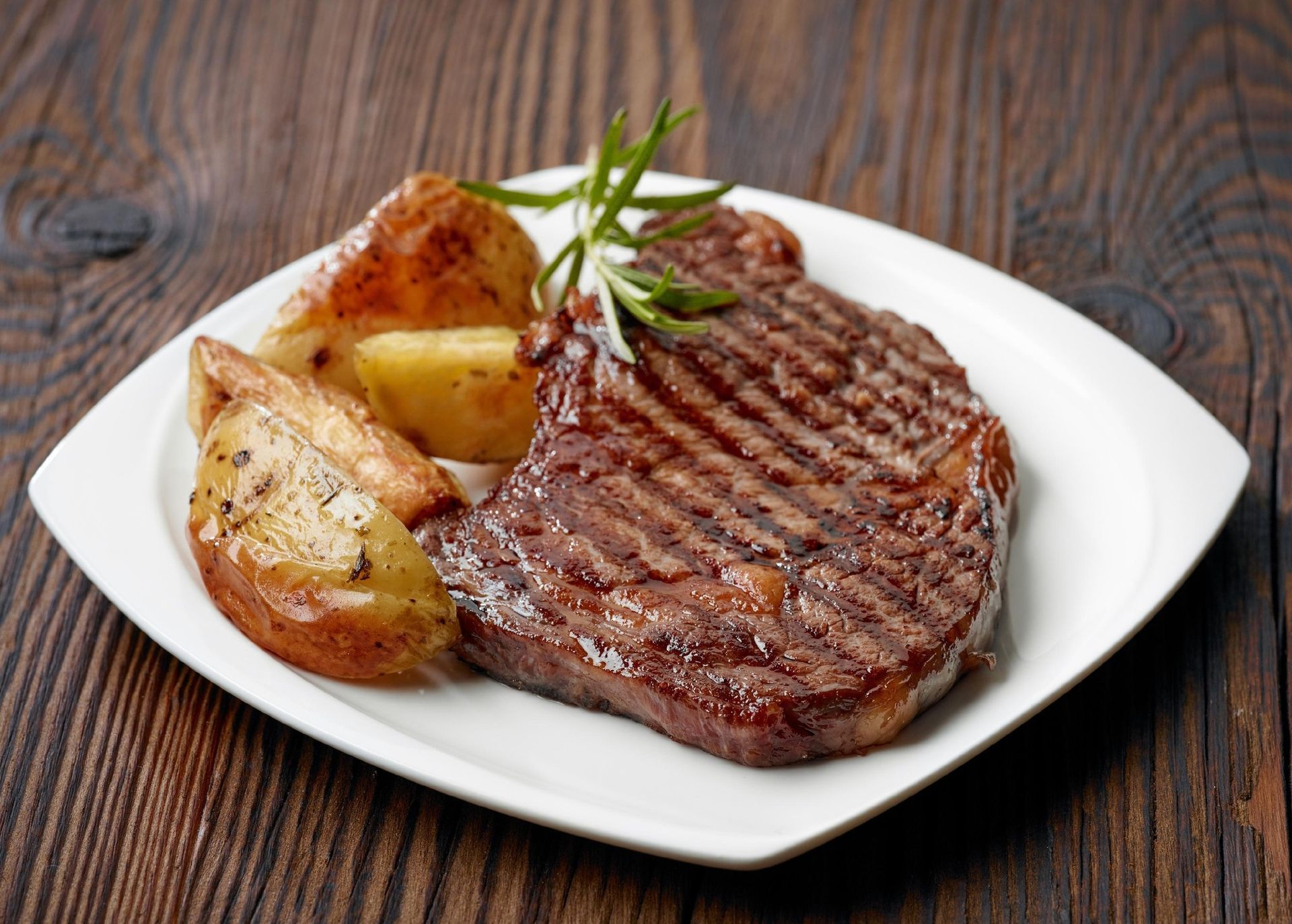 Grilled steak with roasted potato wedges and rosemary on a white plate