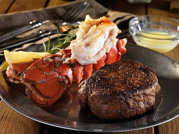 Plated lobster tail and steak with lemon wedge on a dark dinner plate