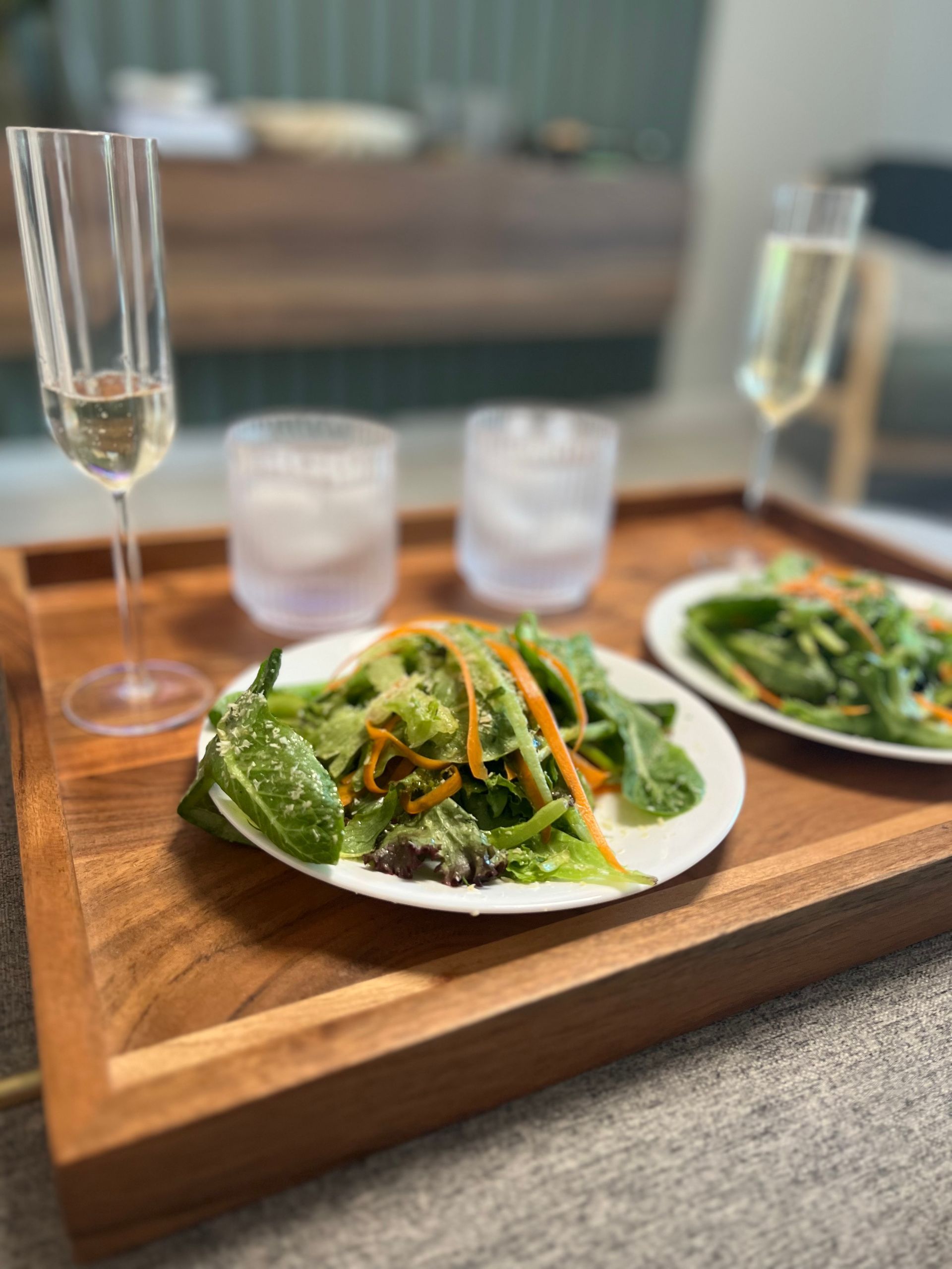Salad on a wooden tray with glasses and water cups on a restaurant table