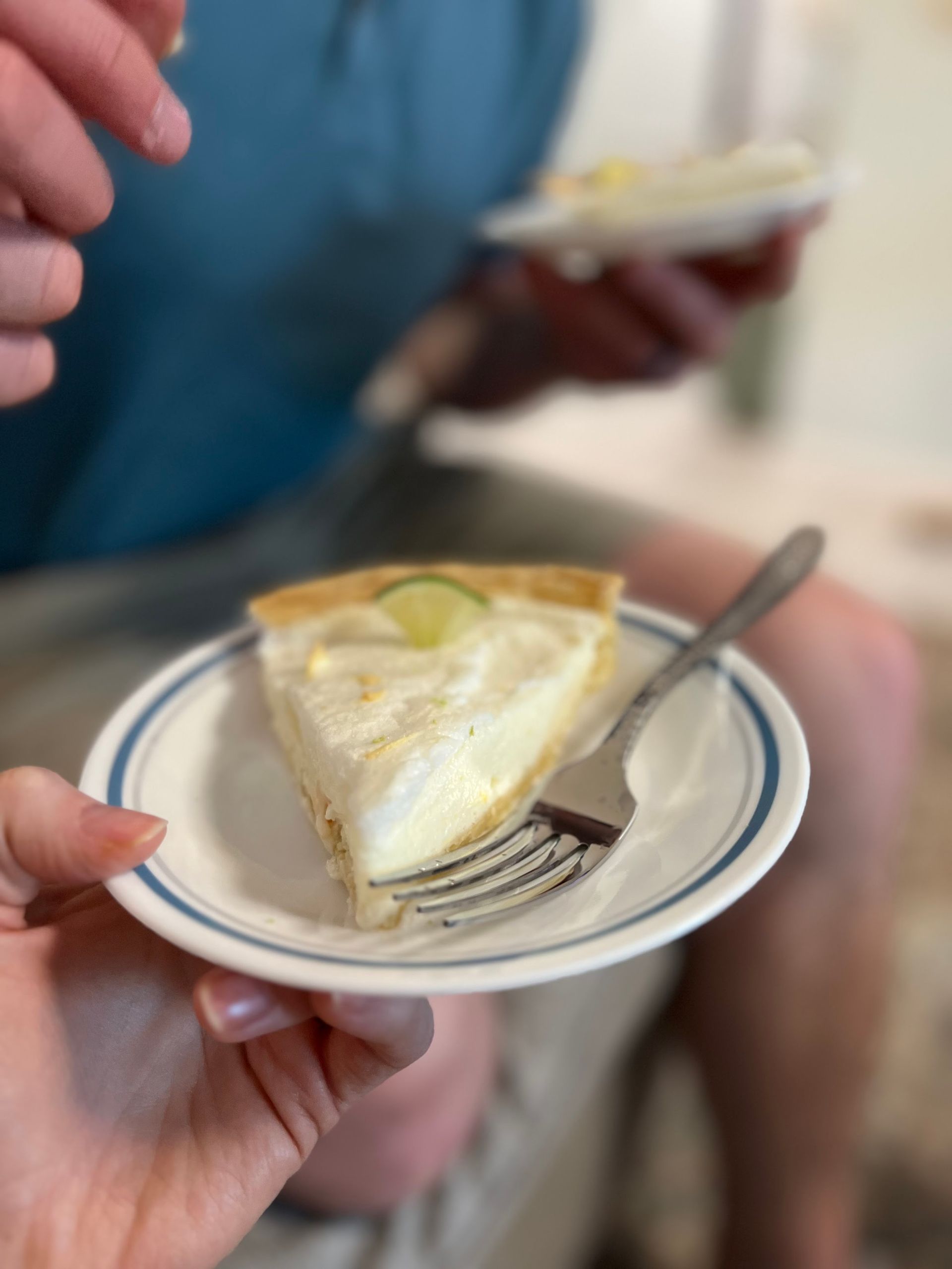 A slice of cream pie on a small plate with a fork, held in a hand at a café table.