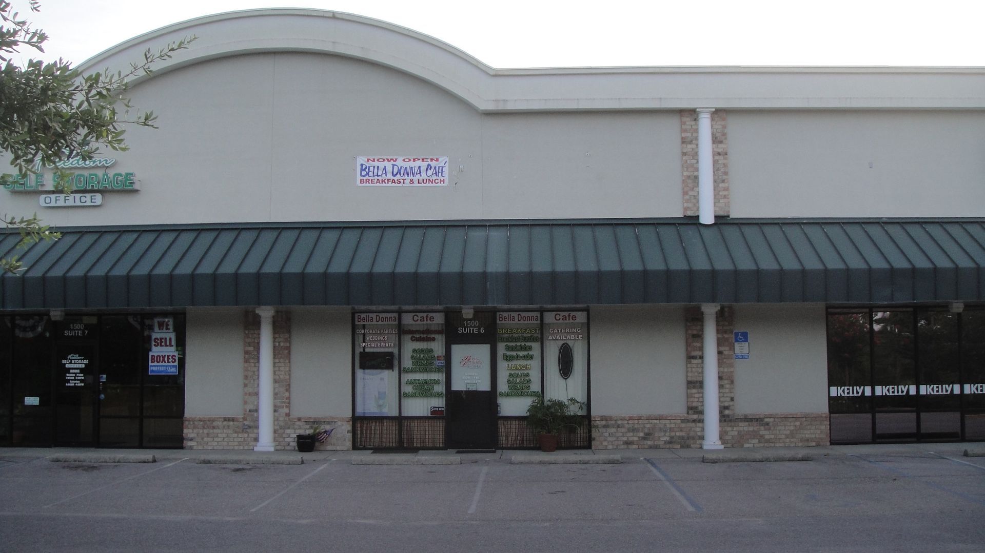 Storefront with a curved white facade, dark awning, and glass entrance in a strip mall.