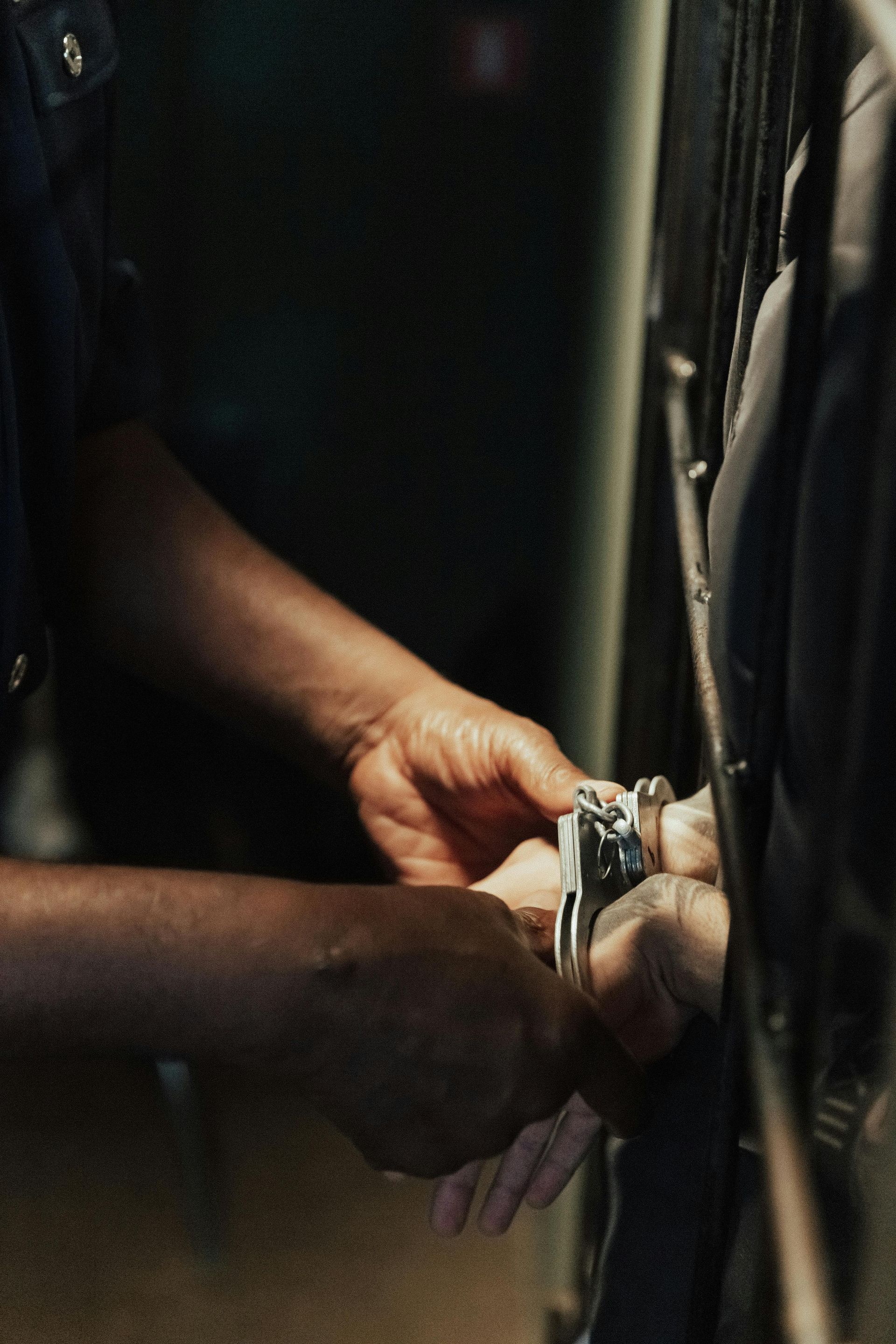 Hands handcuffing a person’s wrists beside a vehicle door in a dark setting