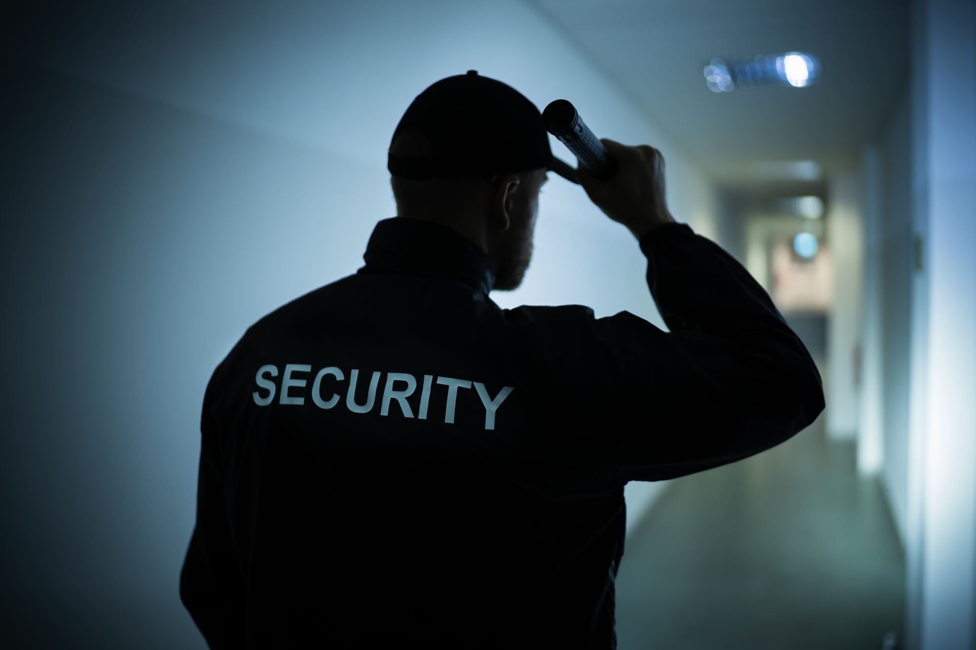 A security guard is looking through binoculars in a dark hallway.