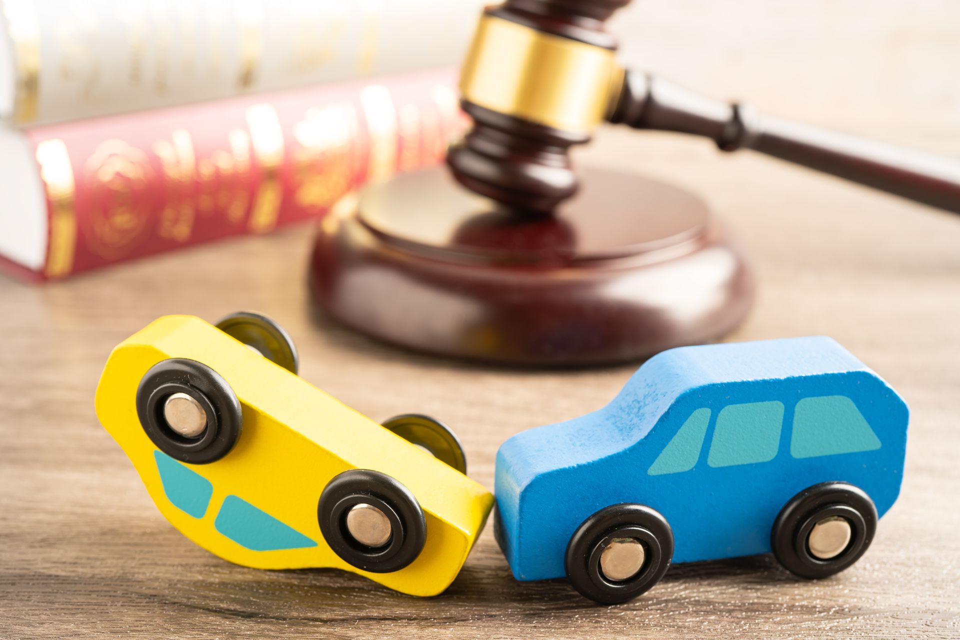 Two wooden cars are sitting on a wooden table next to a judge 's gavel.