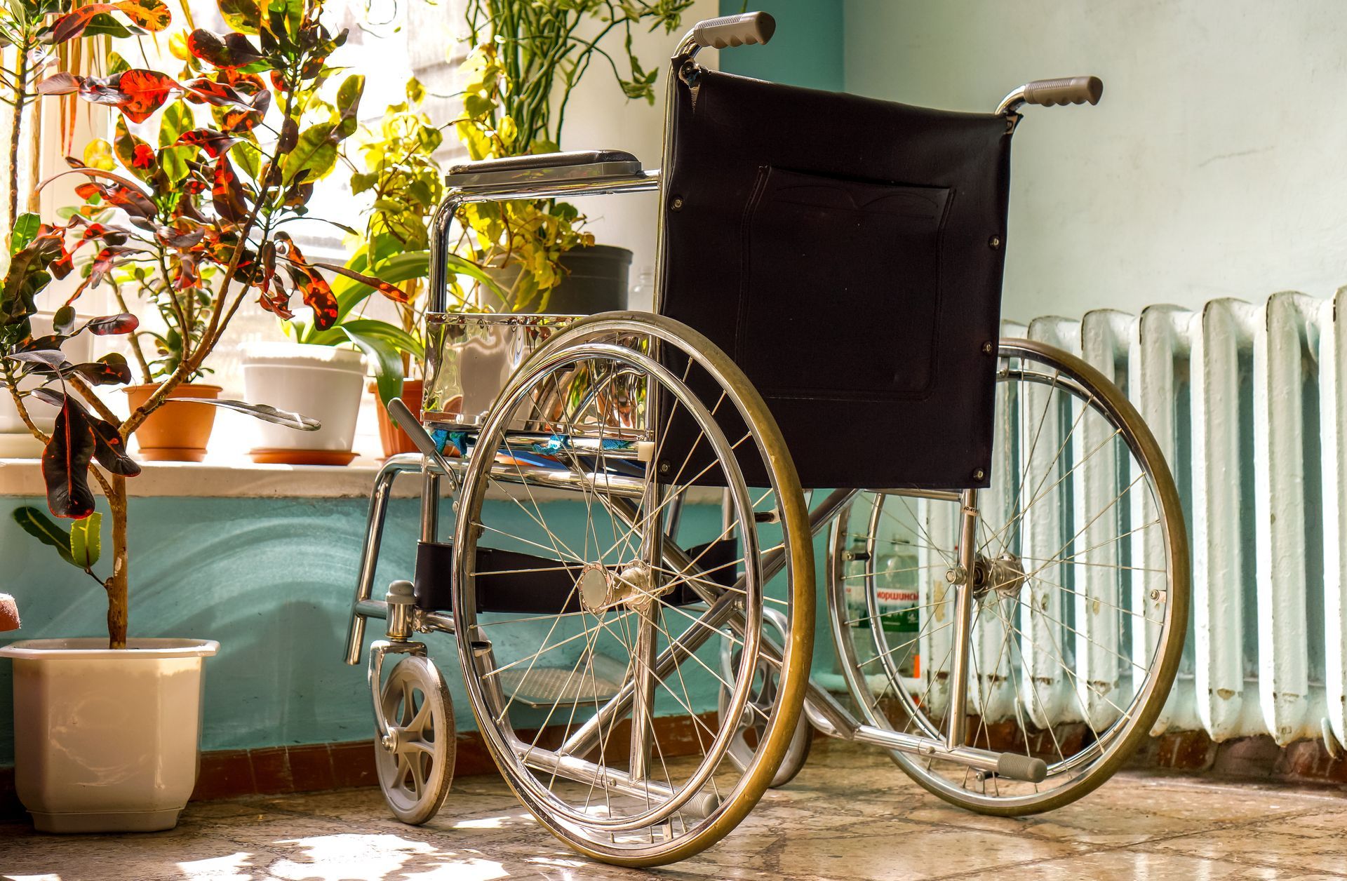 A wheelchair is parked in front of a window next to potted plants.