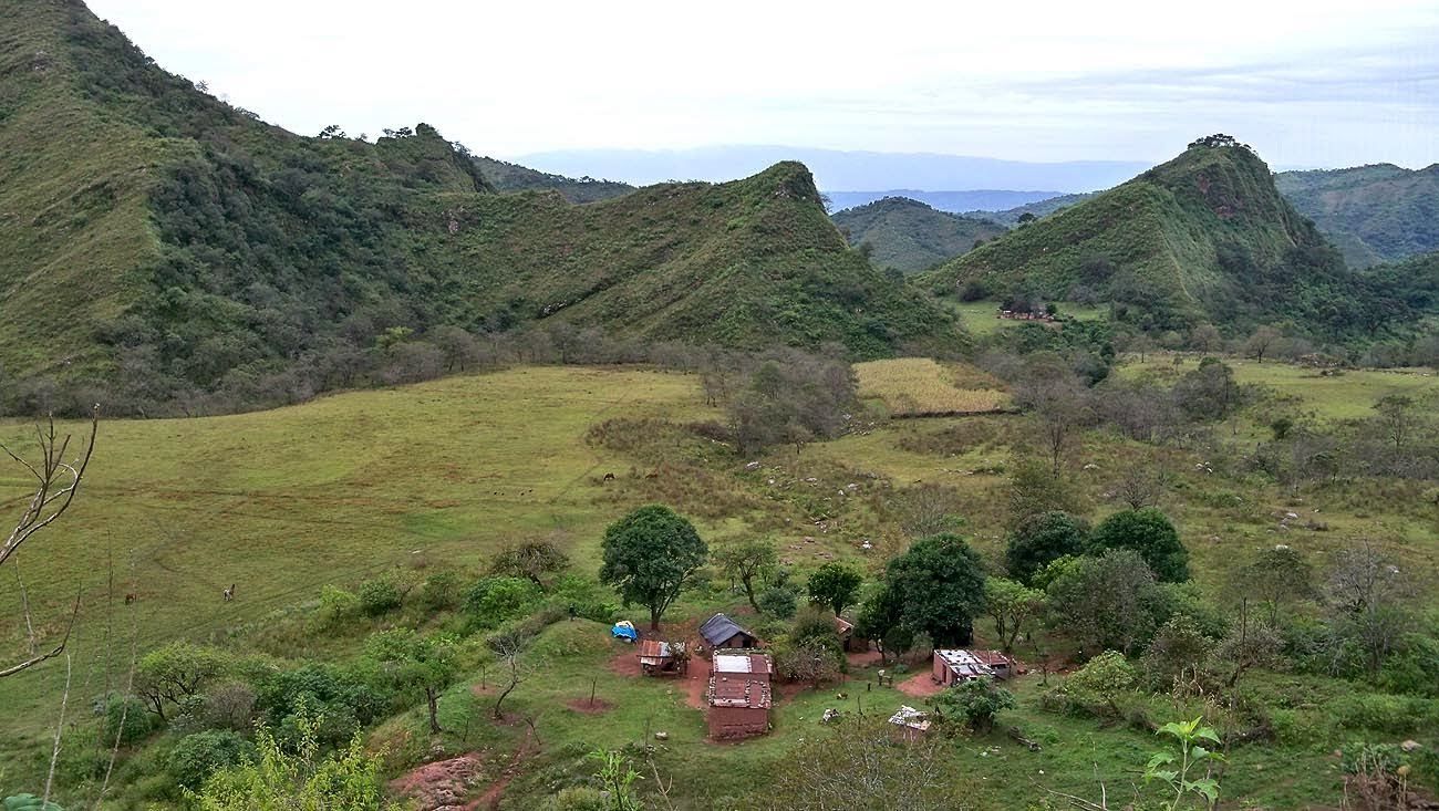 Unas montañas verdes dominan un valle cubierto de hierba con un pequeño campamento y un cielo nublado.