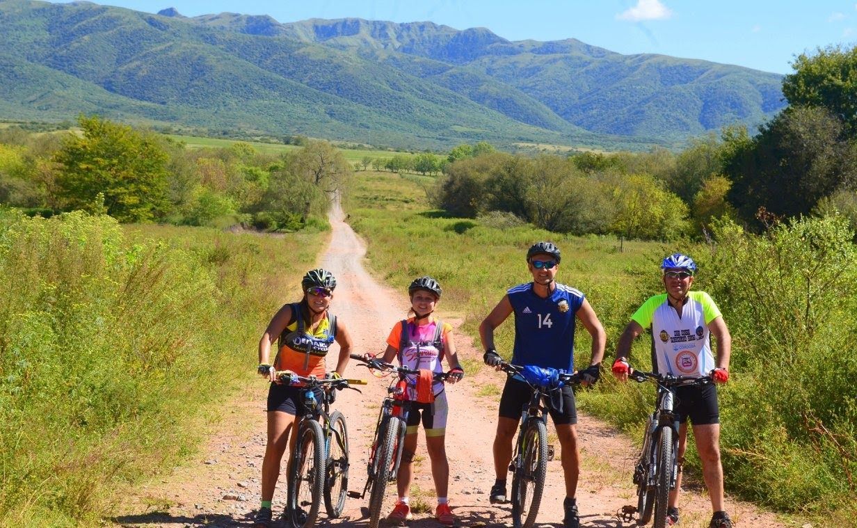 Pampa Grande, bikers recorren  en un camino de tierra, campo verde, montañas al fondo.