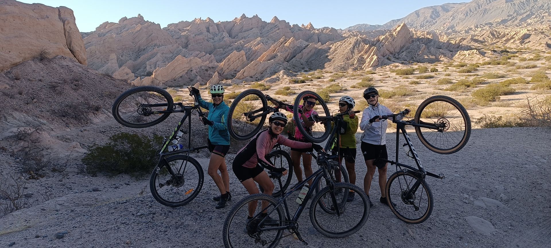 Cinco personas con bicicletas en medio de los Valles calchaquies, algunos levantando sus bicicletas.