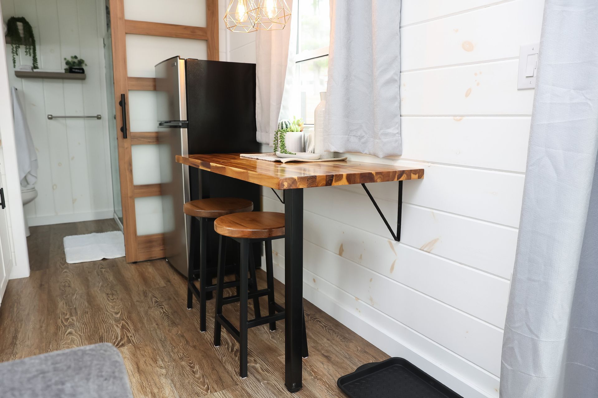 A small kitchen with a table and stools and a refrigerator.